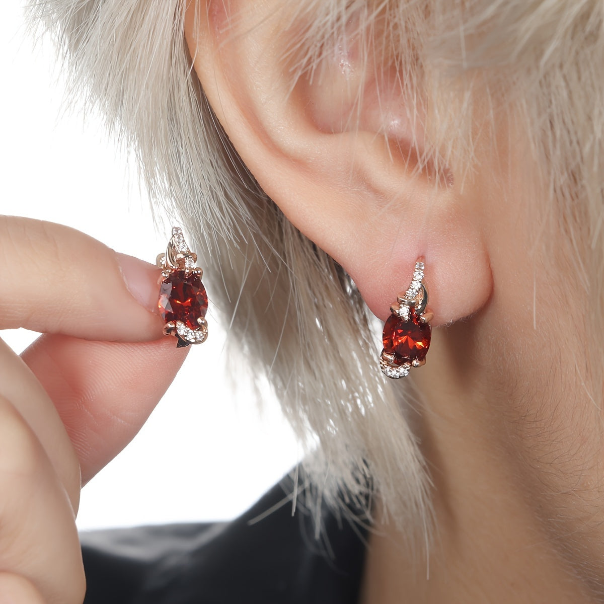Trendy drop earrings featuring red oval-cut stones, elegantly shown on a model's ear.